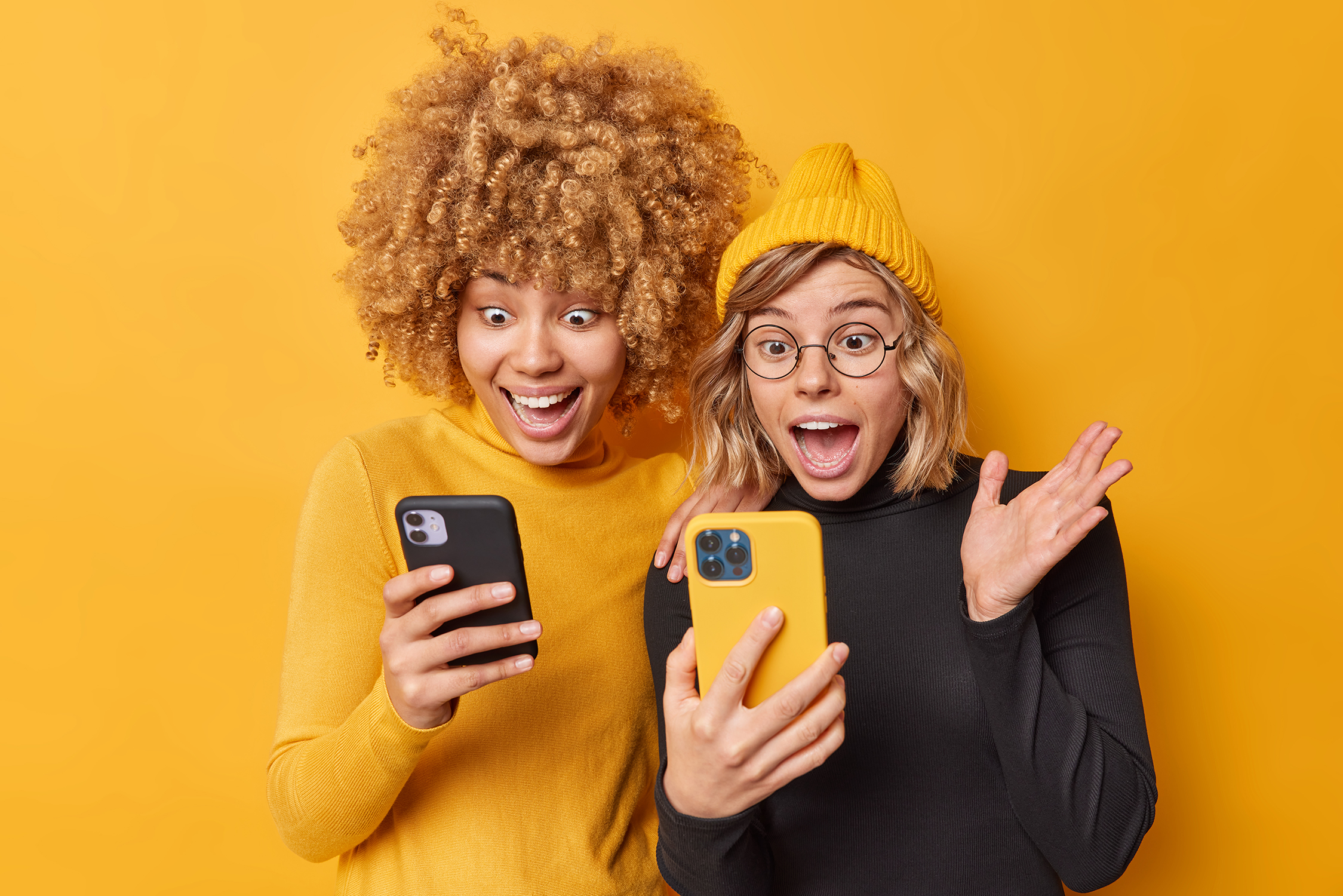iPear technology concept crazy positive women use mobile phones stare screen react amazing news dressed casual turtlenecks isolated yellow wall notice